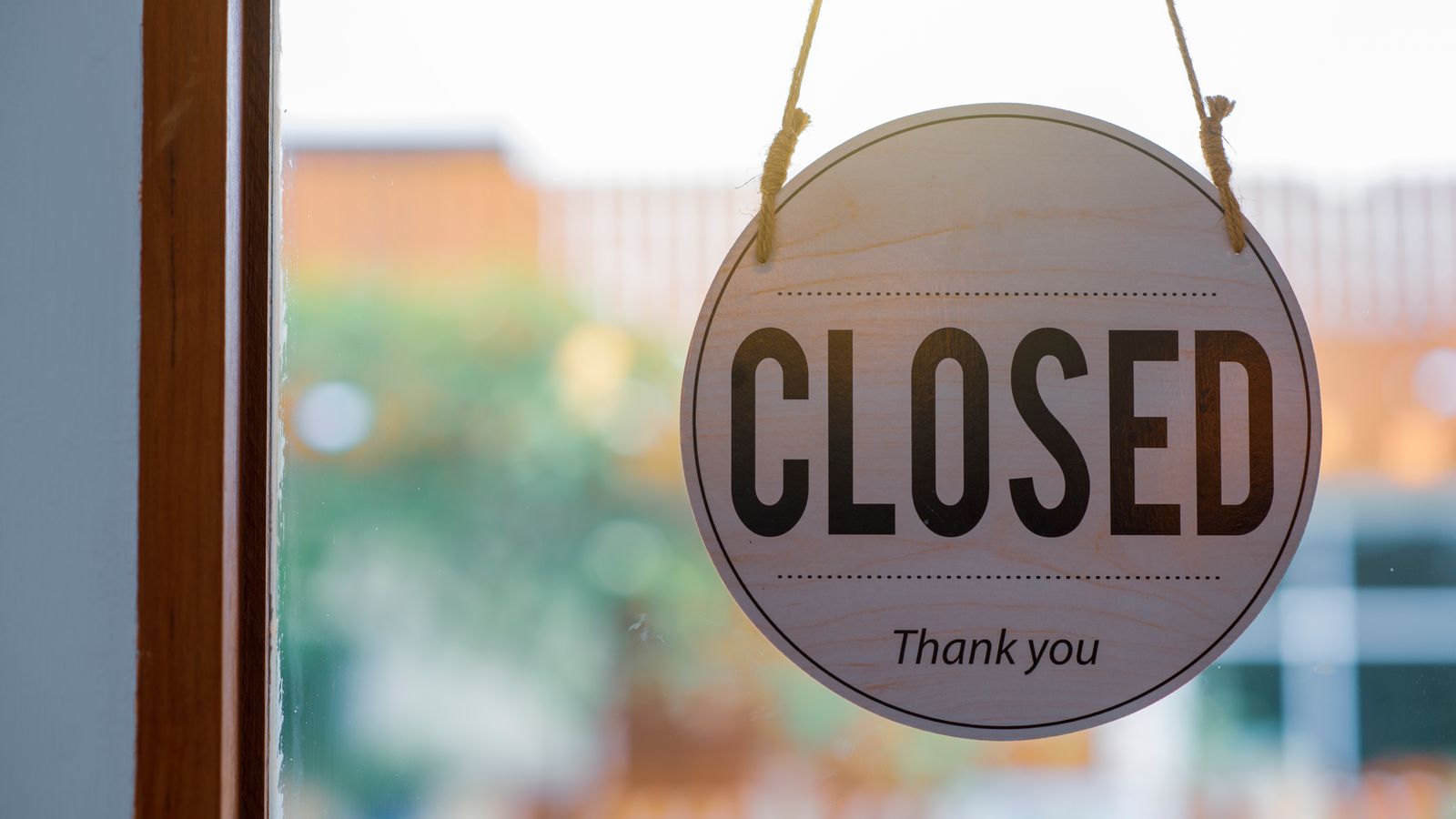 A wooden Closed sign hanging in a shop window