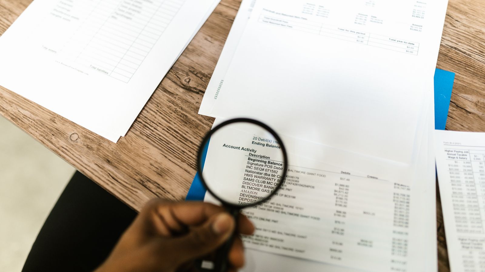 Hand holding a magnifying glass over a set of financial documents