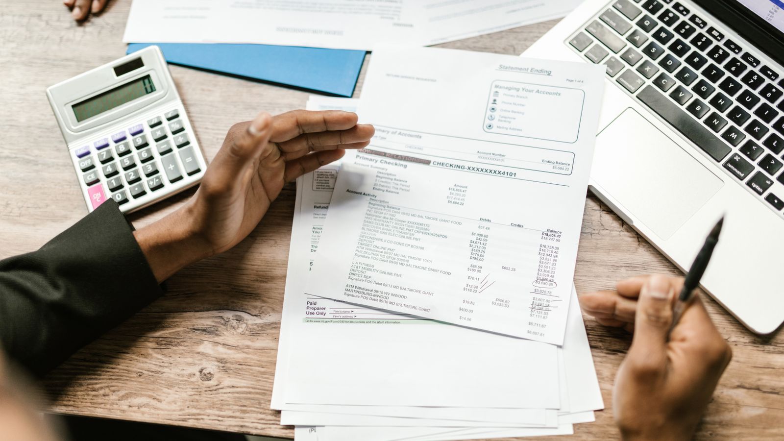 Bank statements checked against a calculator and a laptop on a desk