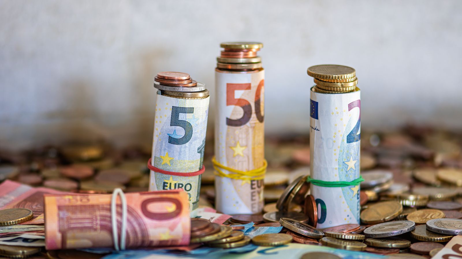 Rolled euro banknotes and coins stacked on a table
