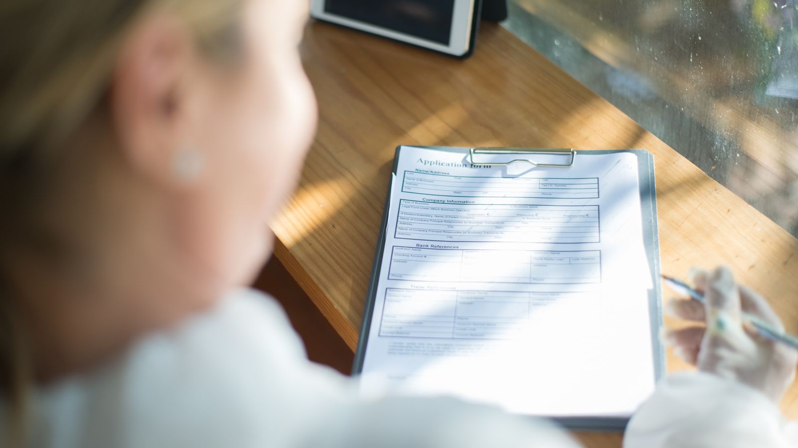 Woman filling in a registration form with a pen at a sunlit desk