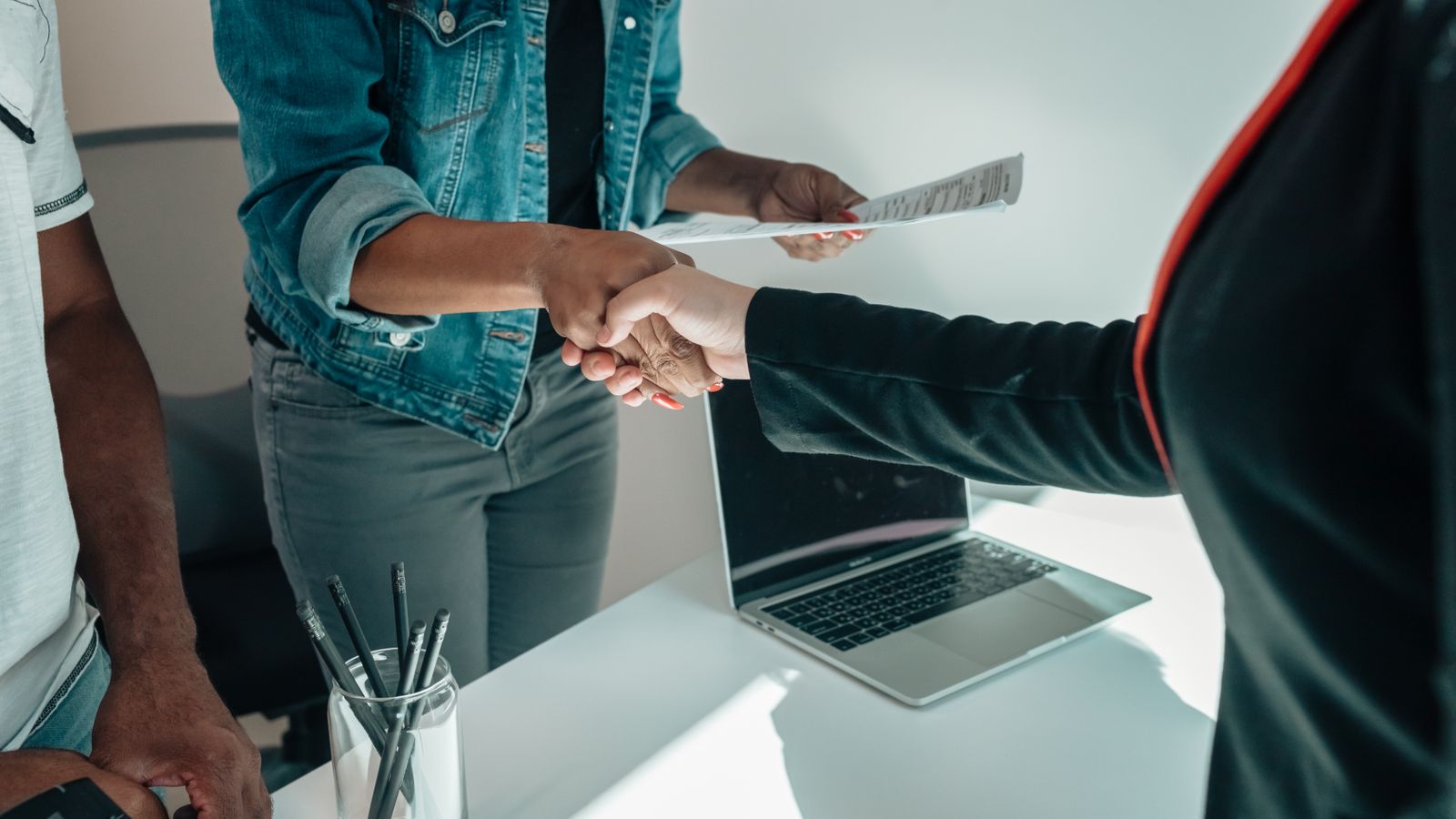 Two people shaking hands across a desk after agreeing terms