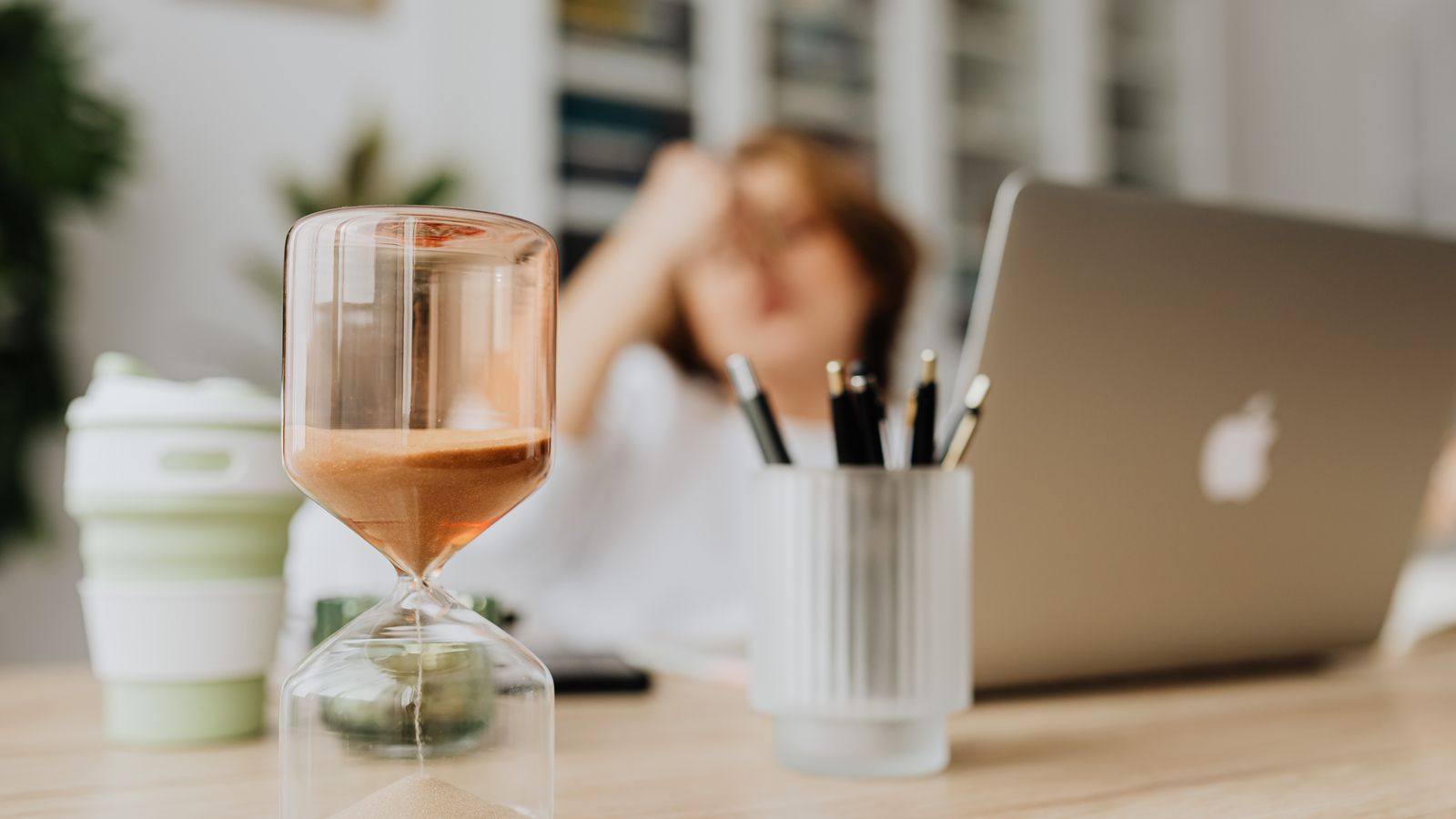 An hourglass running beside a laptop on an office desk