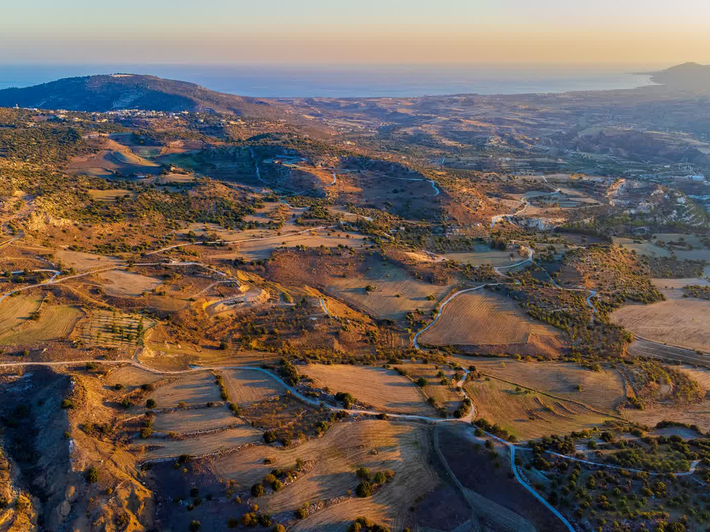 The Cyprus countryside at golden hour from the air, terraced fields and lanes running down to the sea