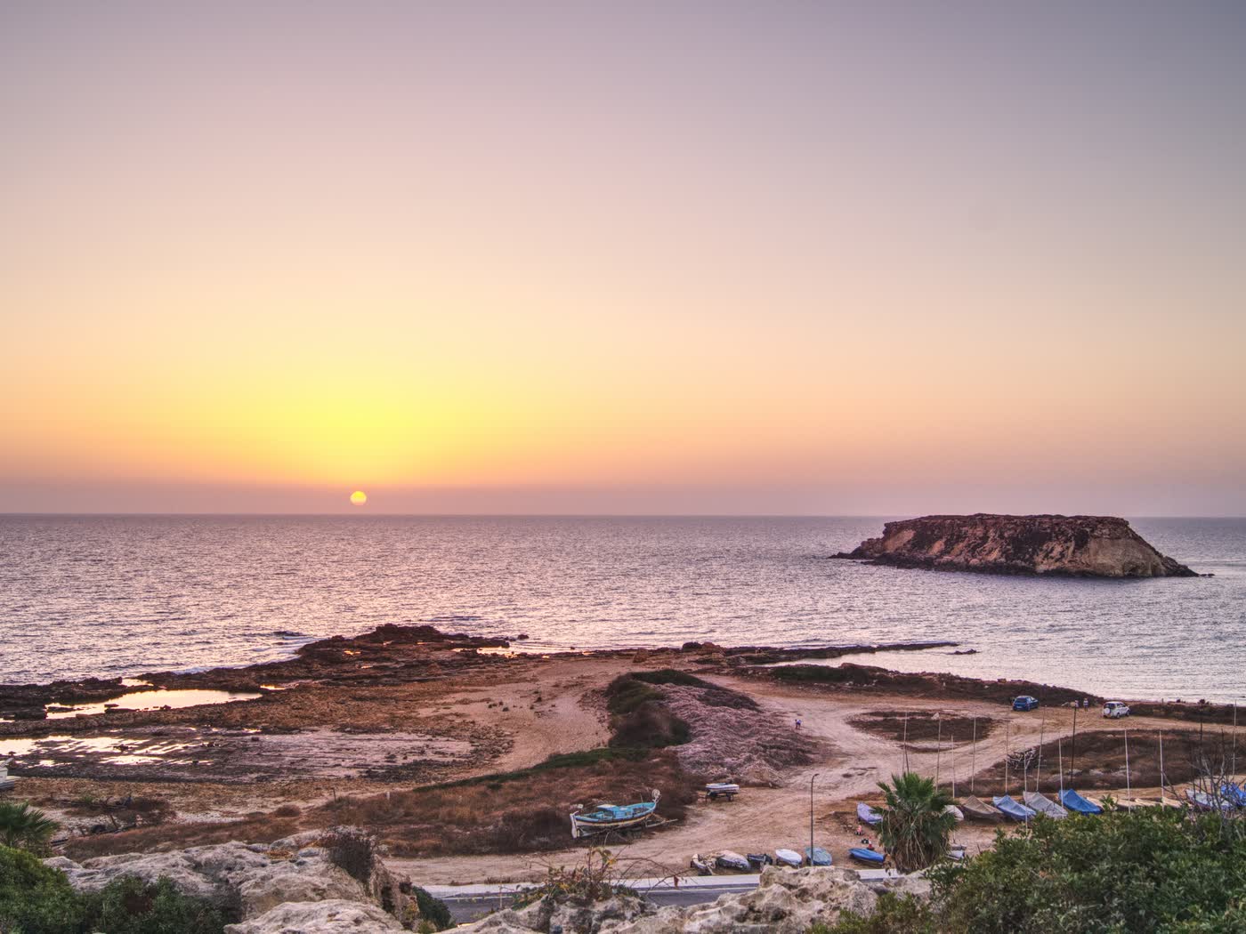 The sun going down behind Geronisos island off the Paphos coast, fishing boats drawn up on the shore
