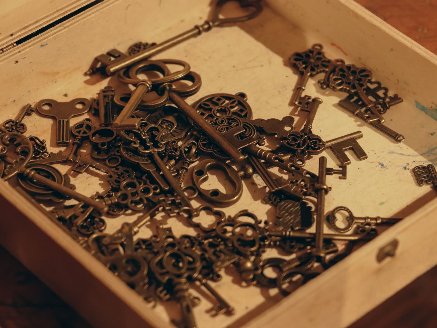 A collection of old brass keys lying in a shallow wooden box in warm lamplight