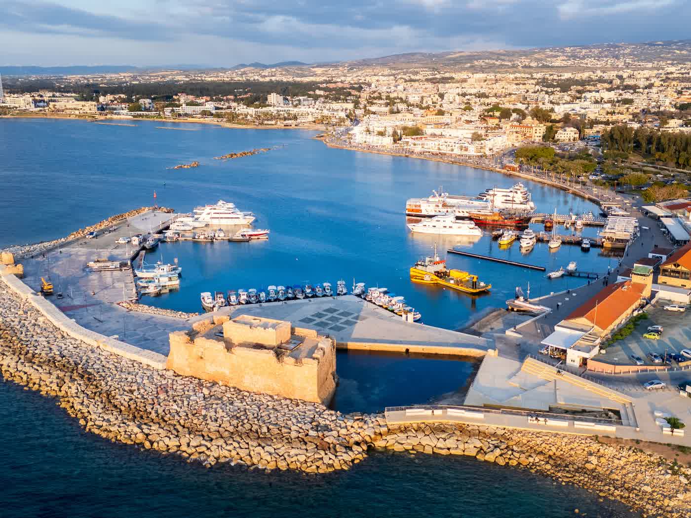Paphos castle and the fishing harbour from the air in late afternoon light, boats moored along the breakwater