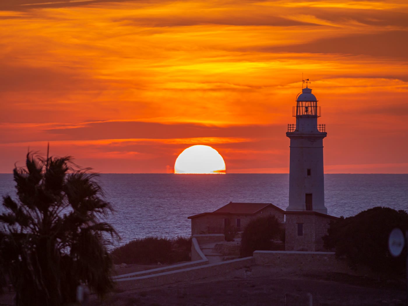 The Paphos lighthouse in silhouette as the sun drops into the sea behind it under a deep orange sky