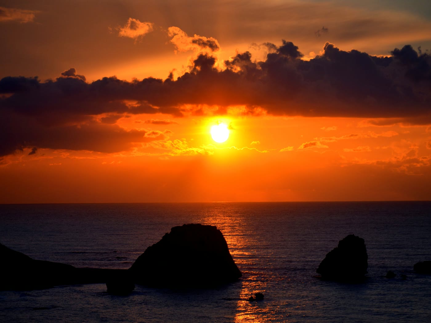 The sun setting into the sea off Cyprus, sea stacks in silhouette under a bank of orange cloud