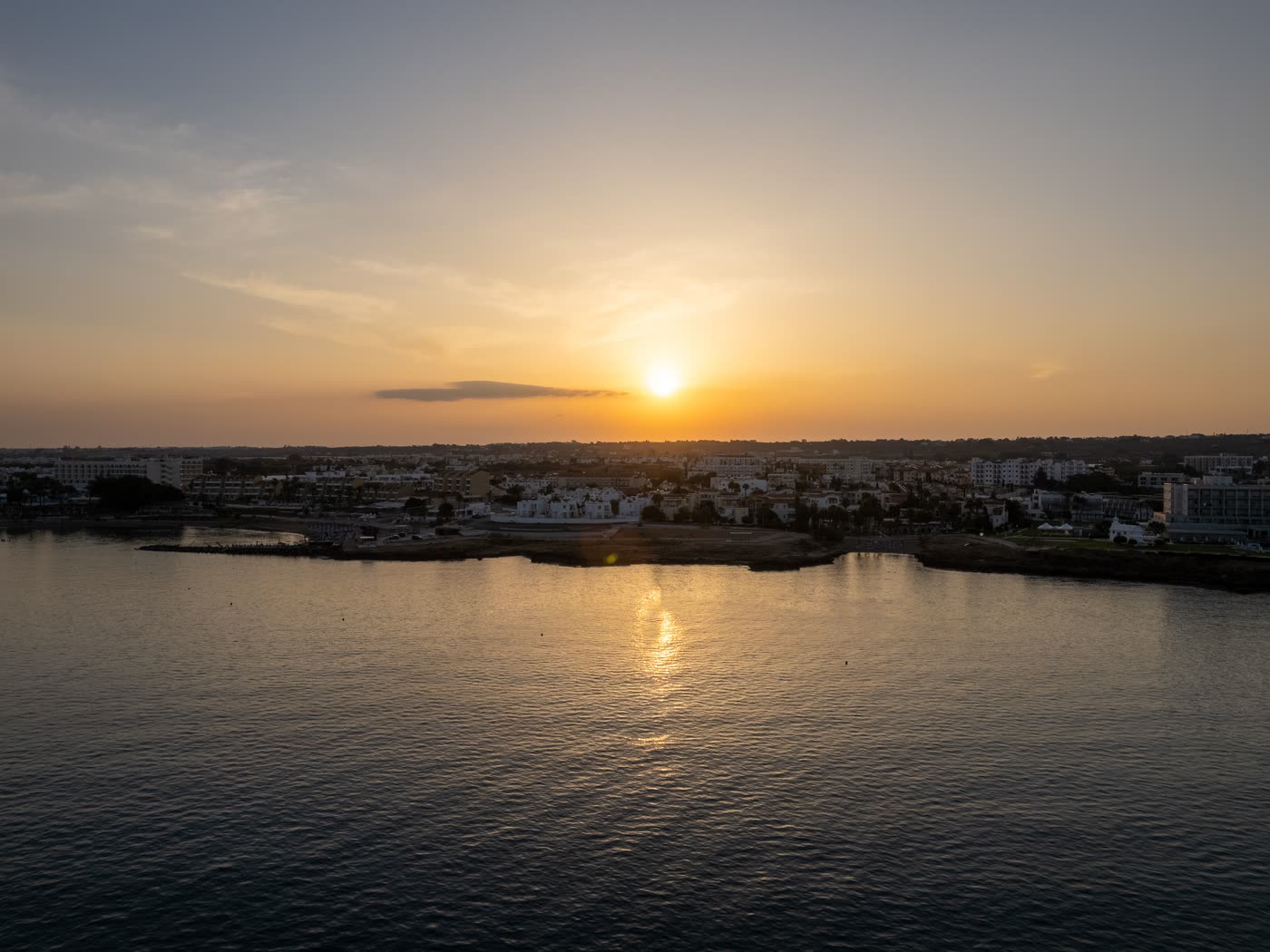 Sunset over a low Cyprus coastal town from the air, the sun's track laid across calm water