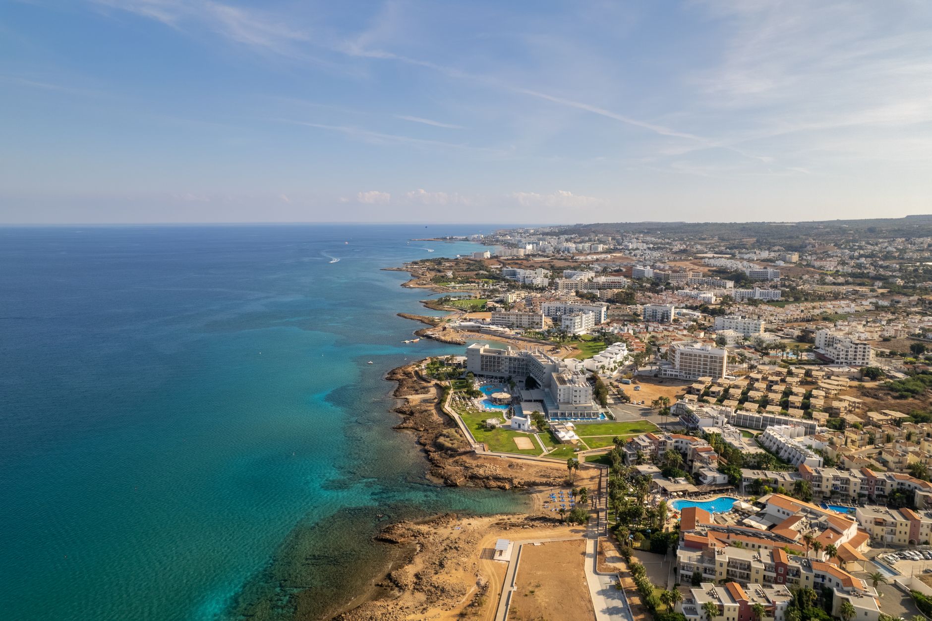 The coastline at Protaras seen from above, with resort buildings along the shore and clear turquoise water in the bays below
