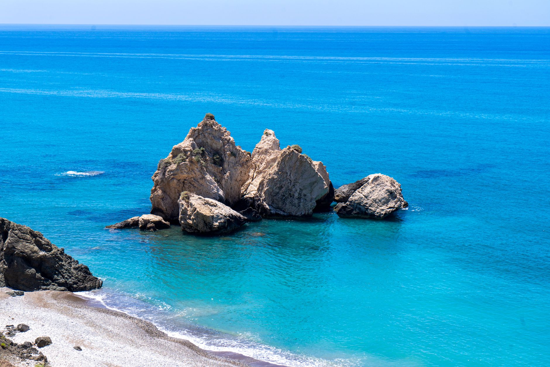 A cluster of pale limestone sea stacks standing in vivid turquoise water off a narrow pebble beach on the Cyprus coast