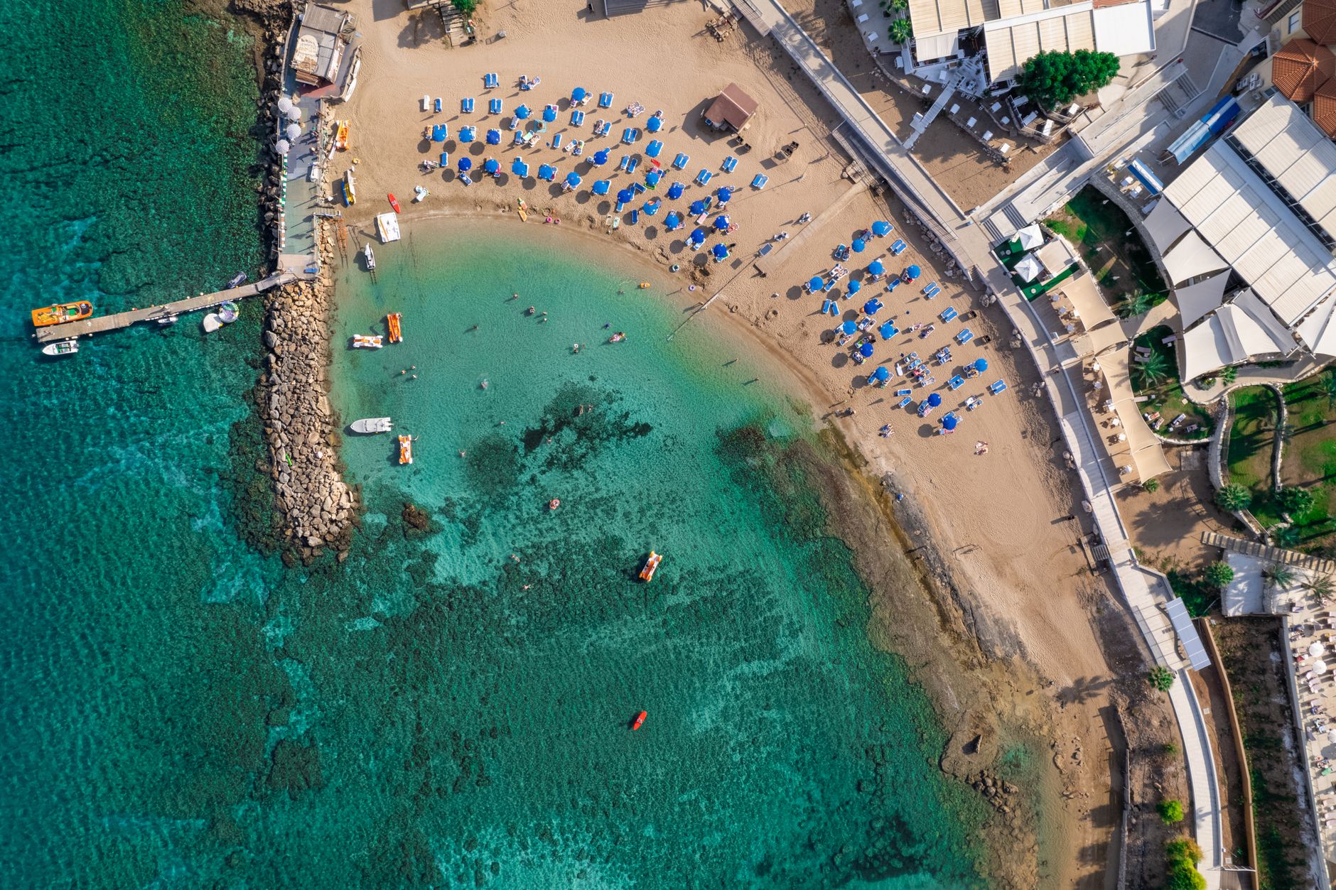 Sunbathers under rows of blue umbrellas on the clear turquoise shallows at Protaras, on the eastern coast of Cyprus