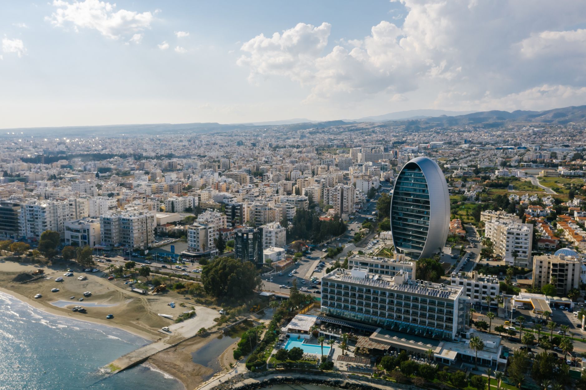 Limassol from the air, with the elliptical Oval tower on the seafront and the Troodos foothills behind the city