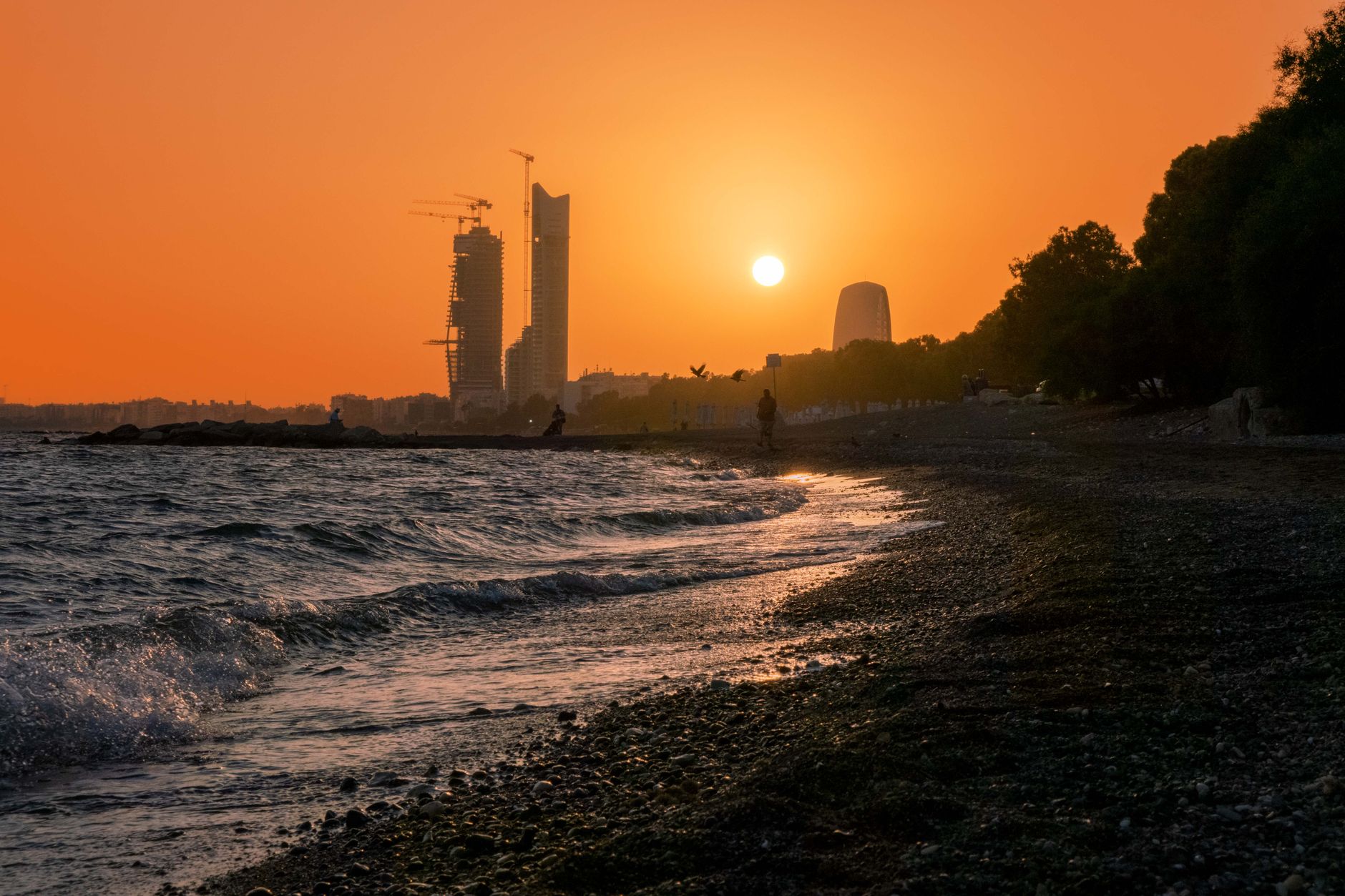 Sunset over the beach in Limassol, with the city skyline standing against an orange sky