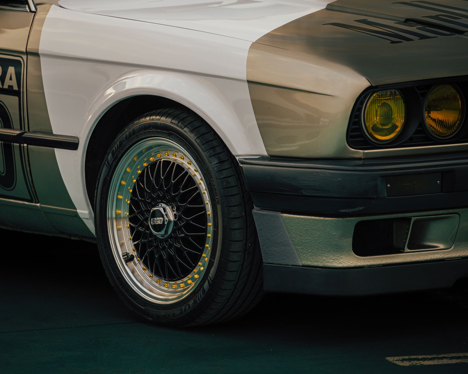 Close-up of the front wing, yellow headlights and polished split-rim wheel of a classic two-tone coupé