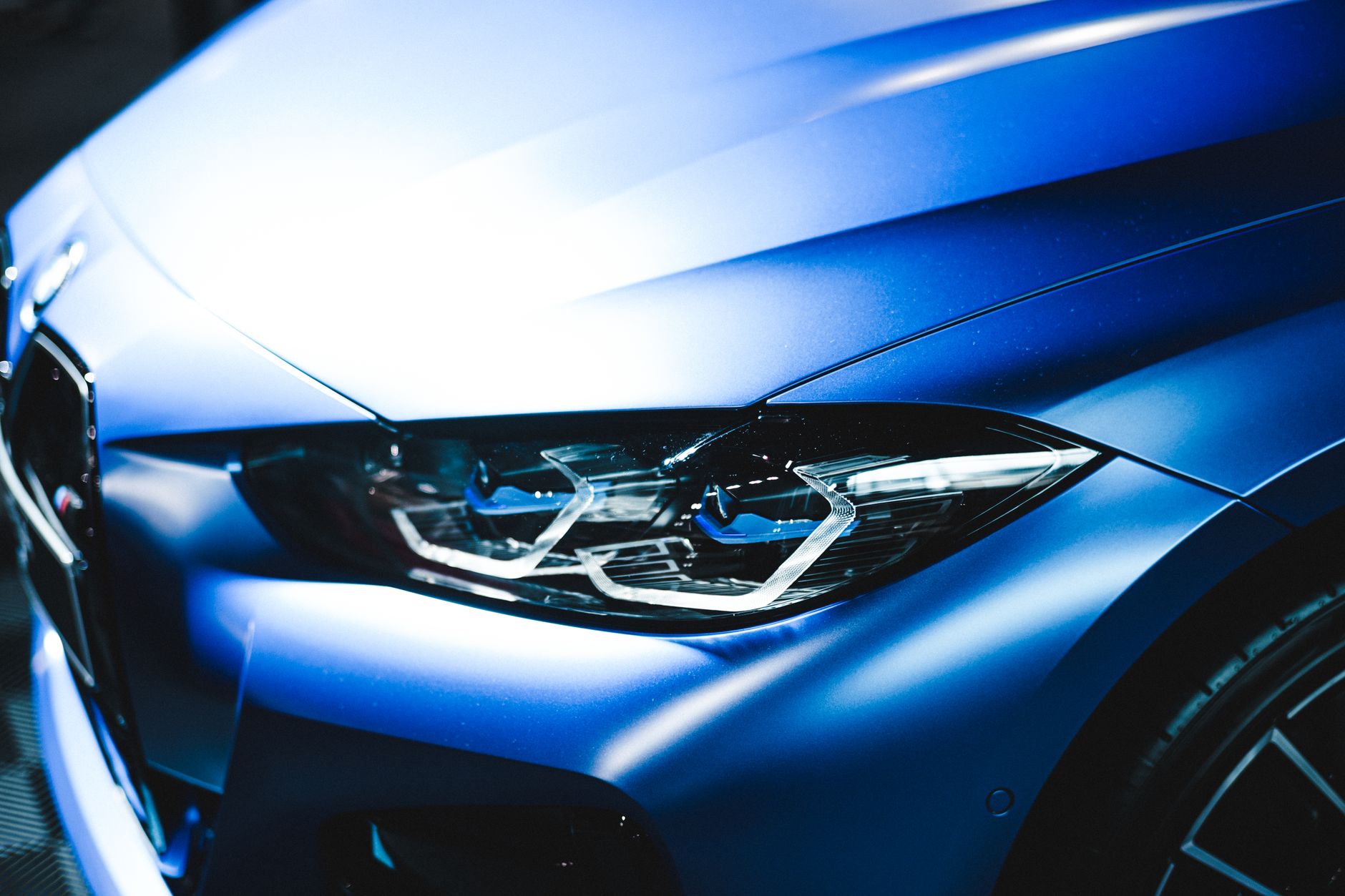 Nærbillede af motorhjelm og LED-forlygte på en mat metalblå sportscoupé mod en mørk baggrund
