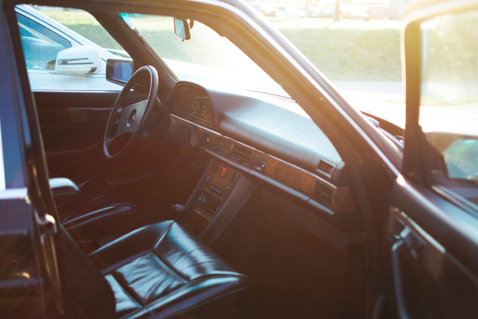The black leather and burl-wood interior of a classic saloon, its door open to warm late-afternoon sunlight