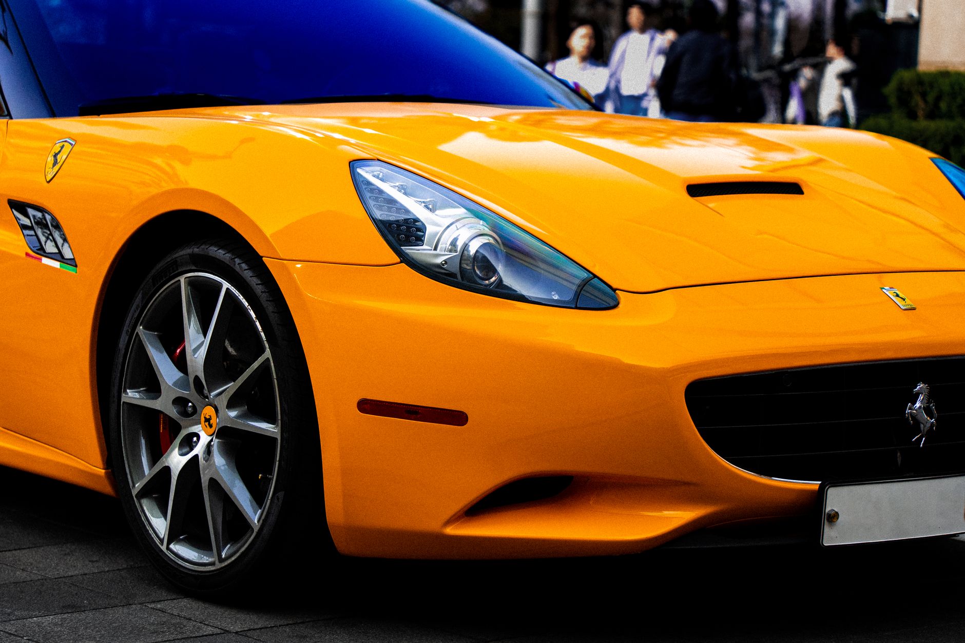 Close-up of the front wing, wheel and headlight of an orange sports car parked on a paved city street