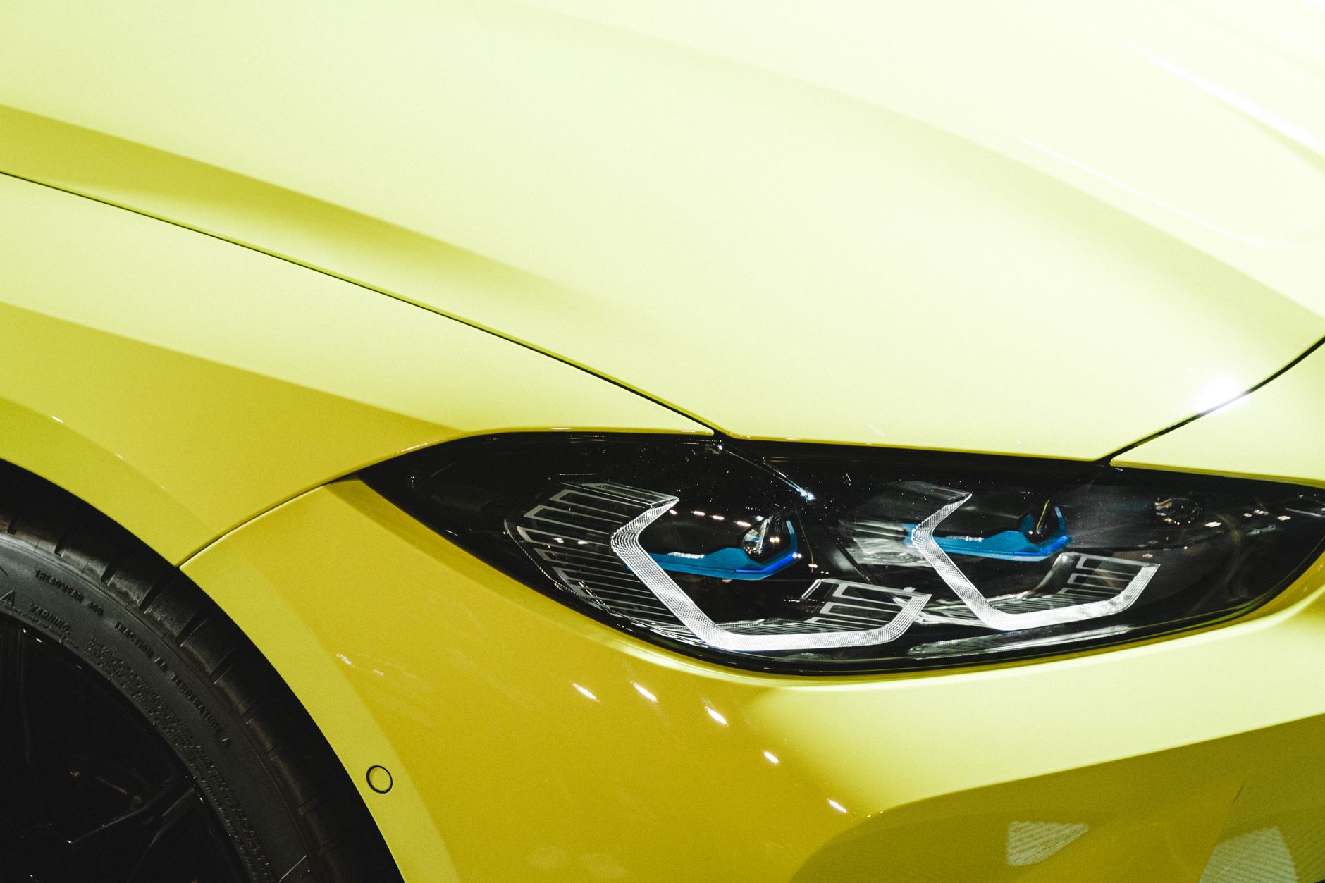 Extreme close-up of the front wing, headlight and part of the front tyre of a lime-yellow sports car under bright indoor lighting