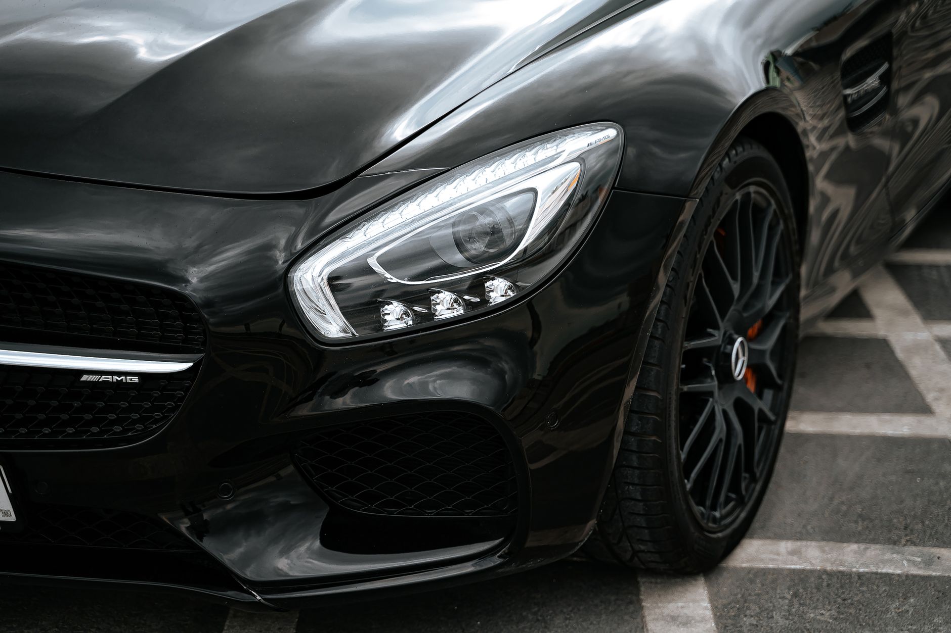 Close-up of the front wing, headlight and black alloy wheel of a polished black sports car parked on light paving
