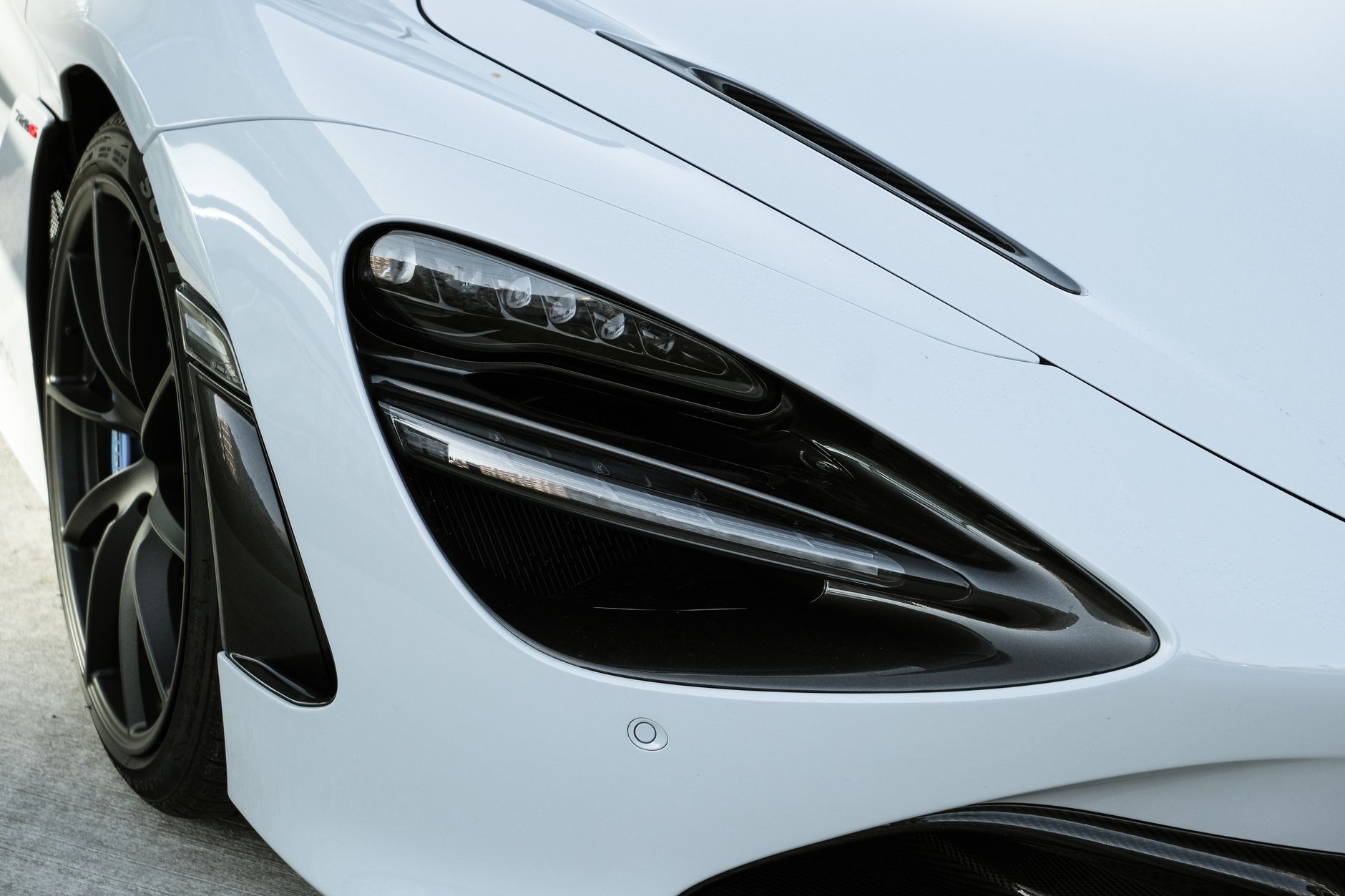 A tight crop of a white supercar’s headlight, front wing and wheel, the bodywork filling the frame