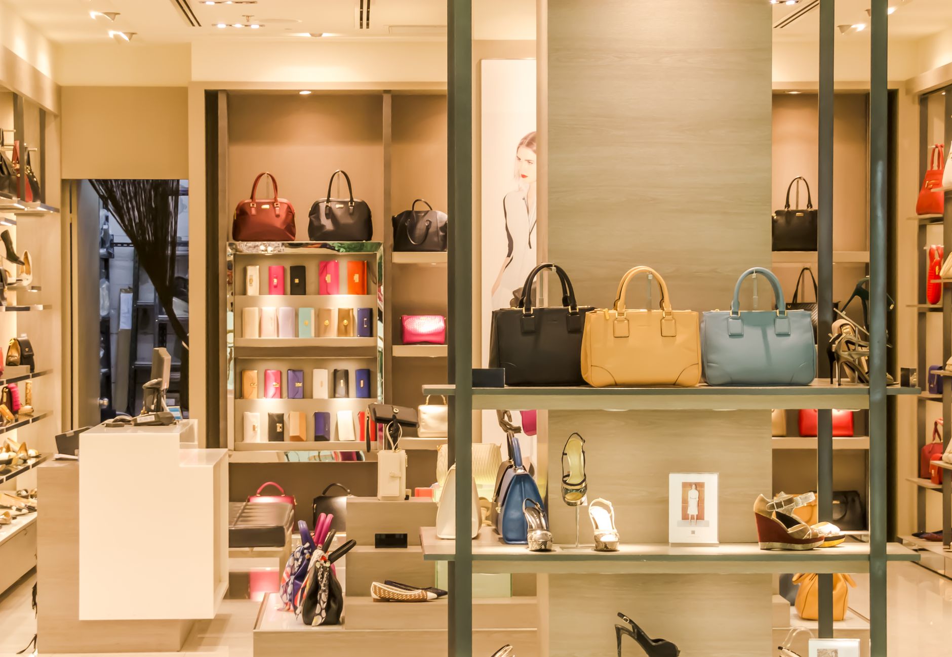 The warmly lit interior of a designer accessories boutique, with handbags, purses and high-heeled shoes arranged on pale wooden shelving