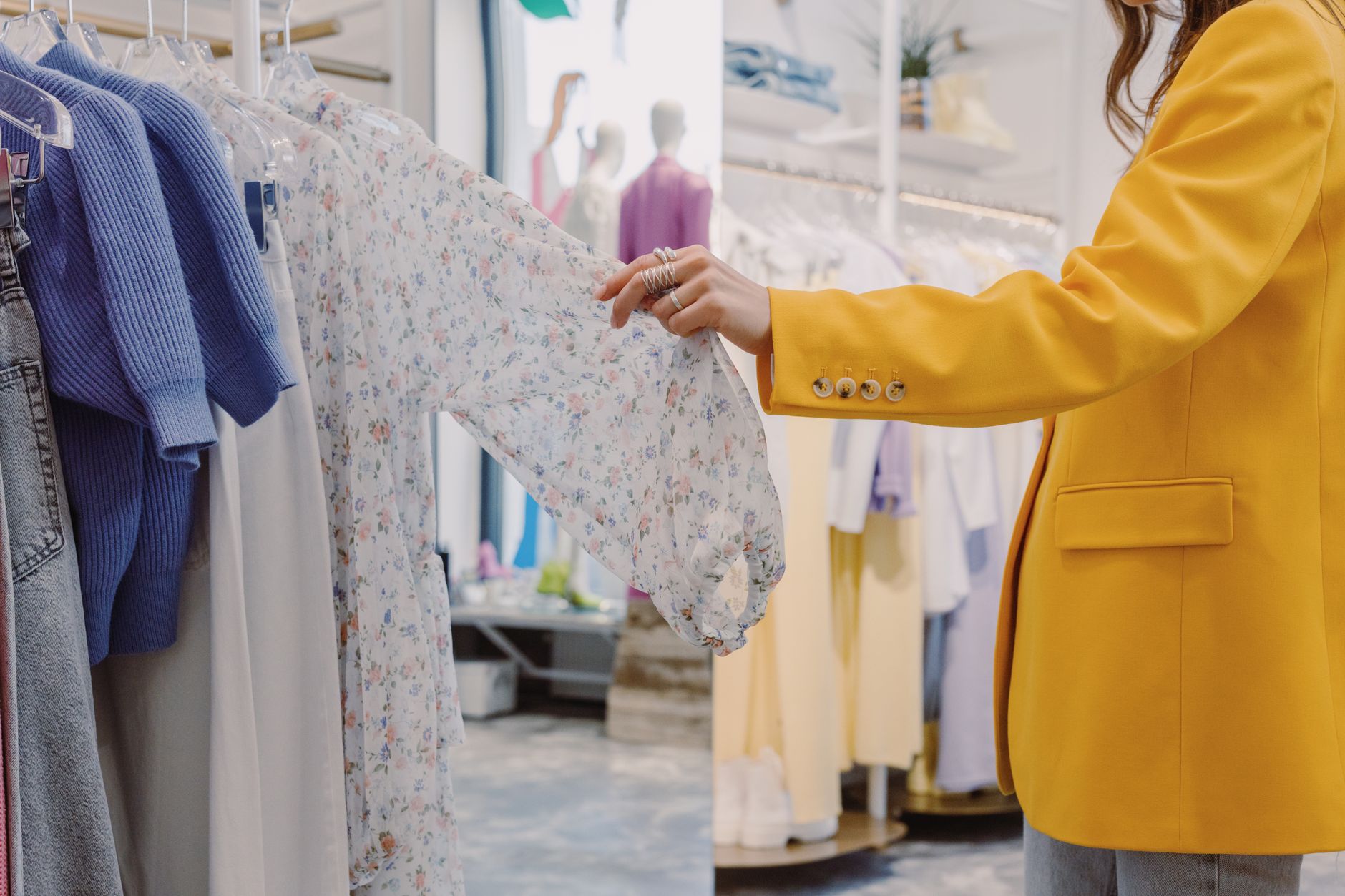 A woman in a yellow tailored blazer looking through a rail of clothes in a bright modern boutique